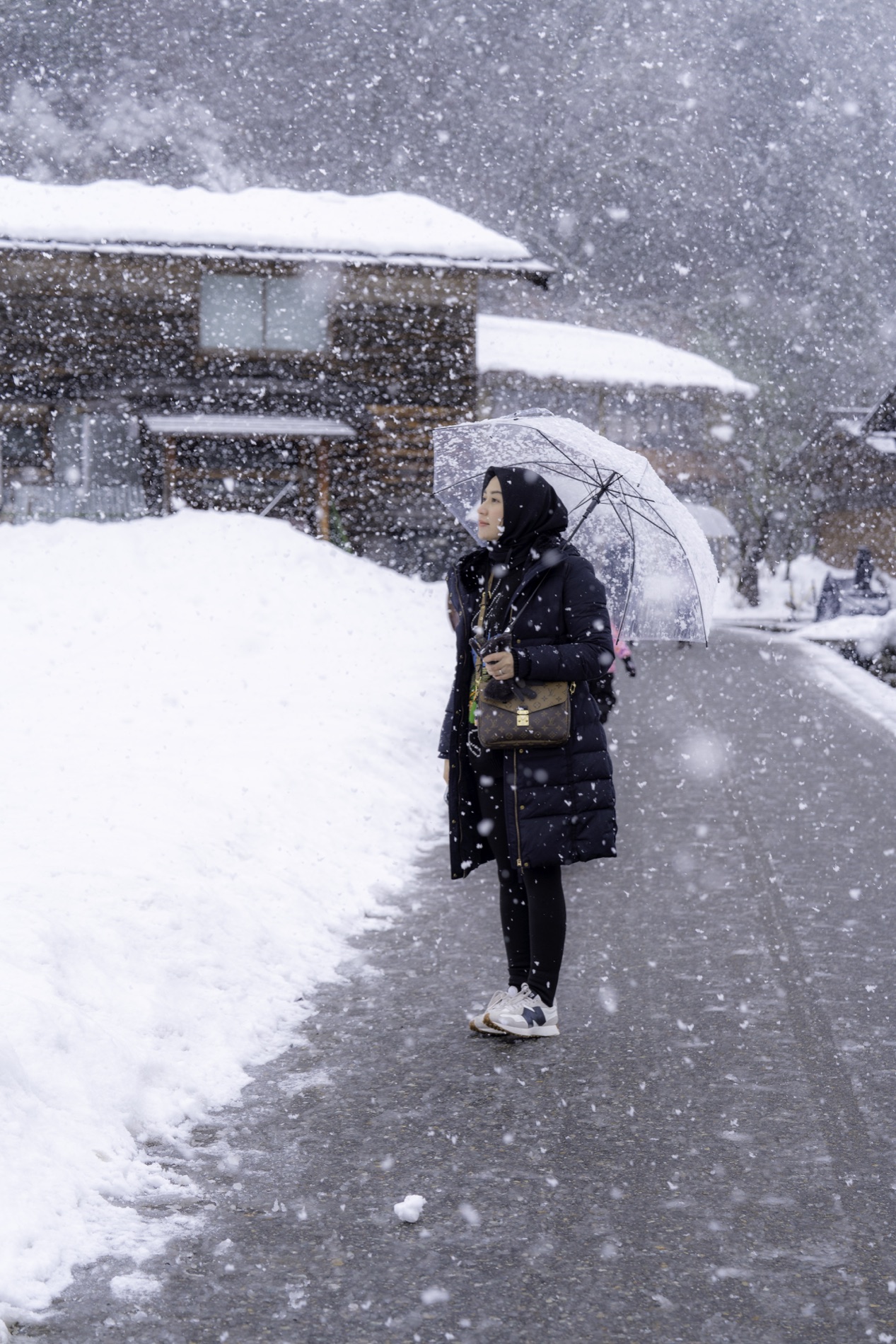 Traveler with a clear umbrella during snowfall in a historic Japanese village
